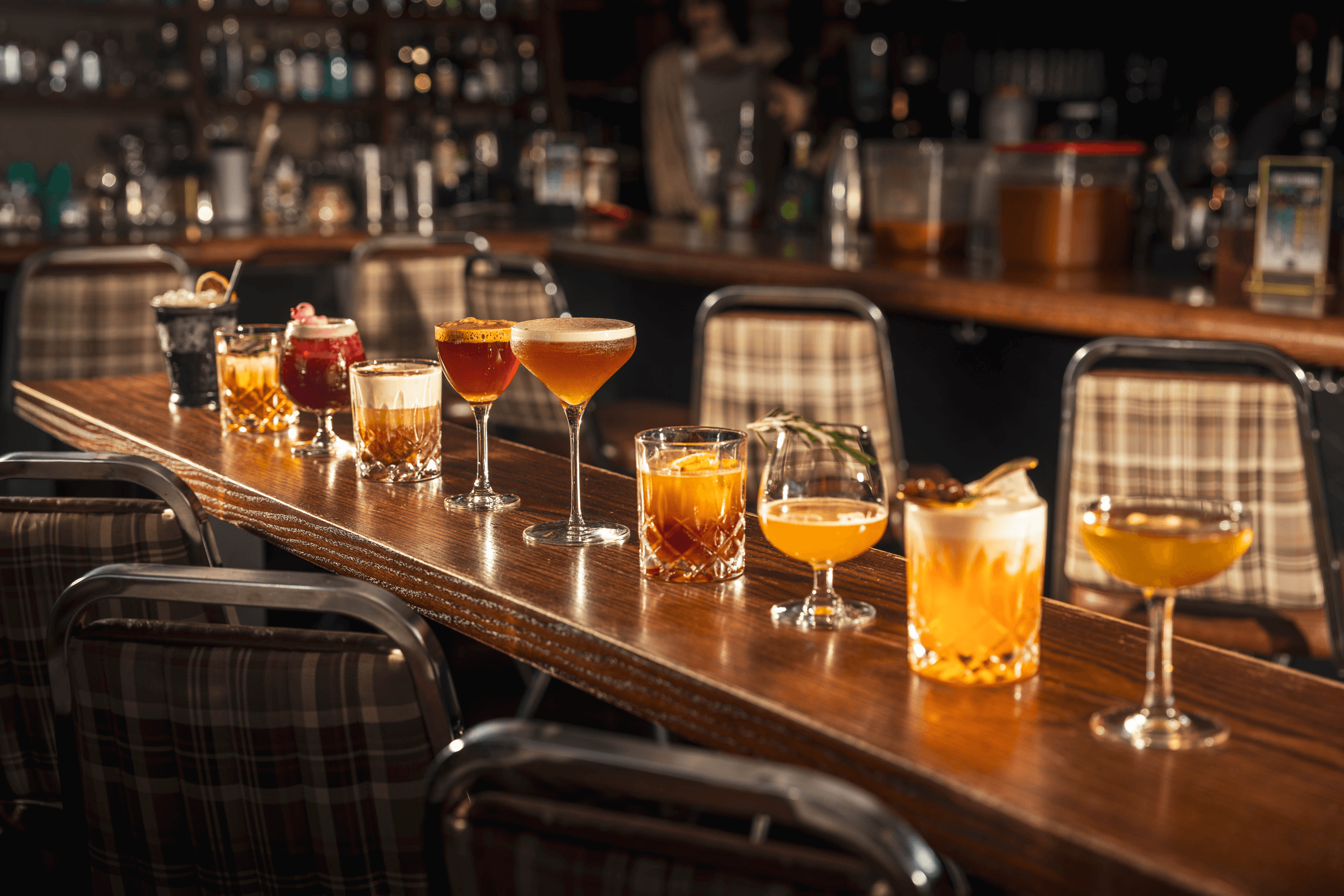 A vibrant row of crafted cocktails in elegant glassware gleams against a polished wooden bar, inviting a luxurious experience.
